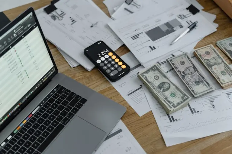 open laptop with a calculator on top of paperwork and stacks of cash for custom quotes.